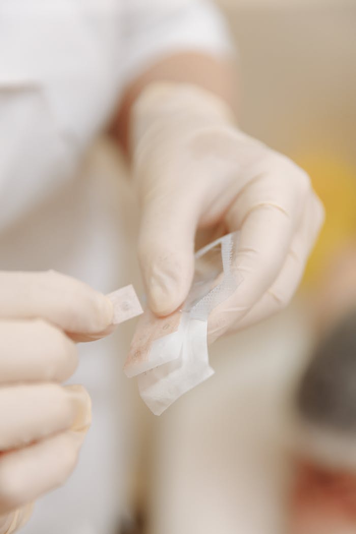 Close-up of hands wearing latex gloves applying a sterile bandage.